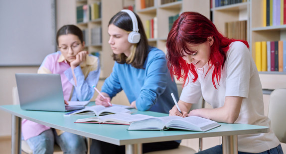 Gruppe von Teenagern lernt an ihren Schreibtischen im Bibliotheksunterricht. Teenager schreiben in Notizbüchern mit Büchern Laptop.